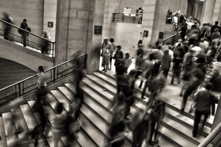 Greyscale photo of people in suits going up and down stairs, slightly blurred like they're moving too quickly for the photographer to capture